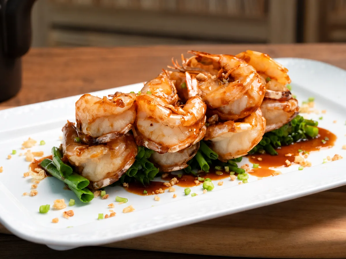 Pan-fried crystal prawns glazed in a glossy oyster sauce on spring onions, served on a white plate