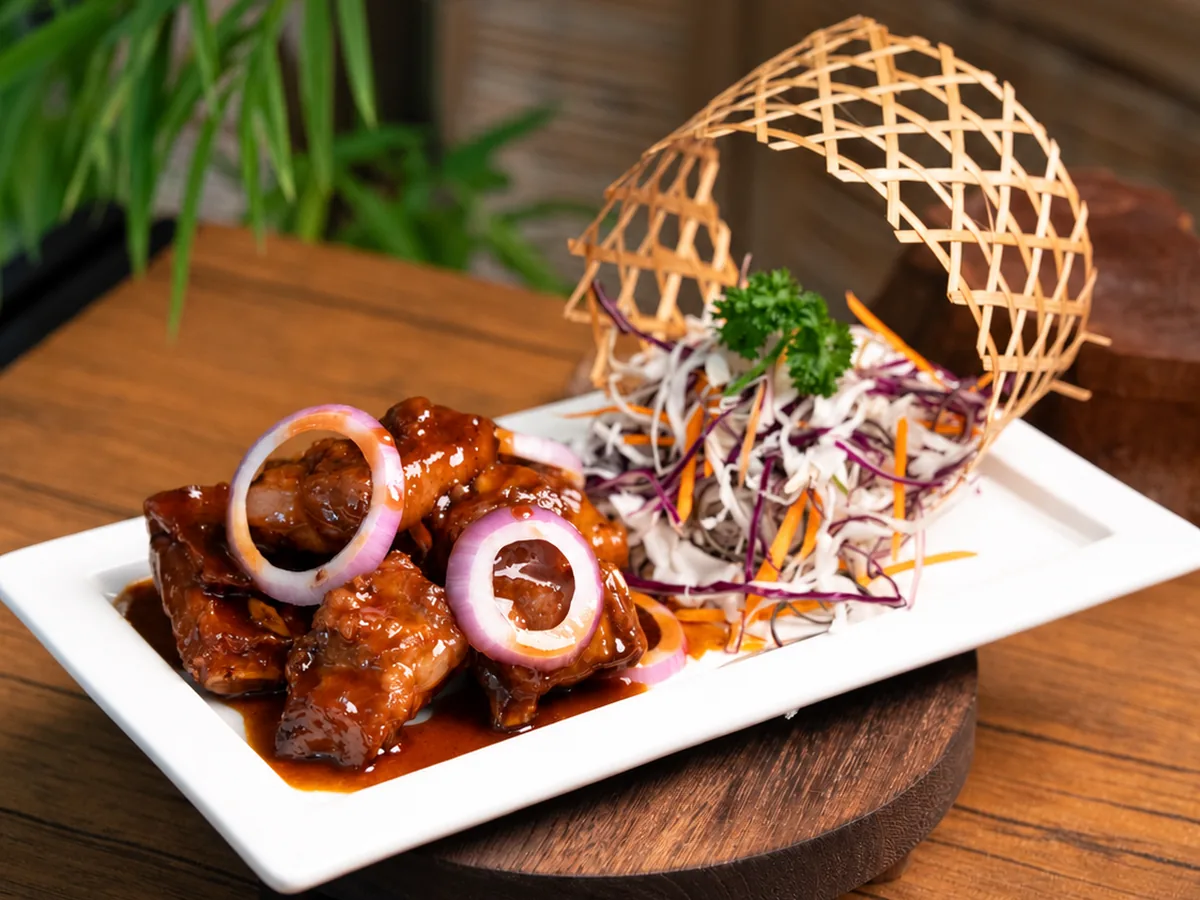Deep-fried pork ribs with red onion rings in a glossy vinegar sauce, served with shredded cabbage on a white plate